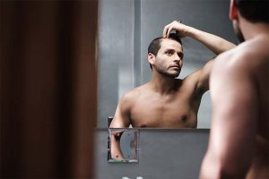 hombre revisando su cuero cabelludo frente al espejo