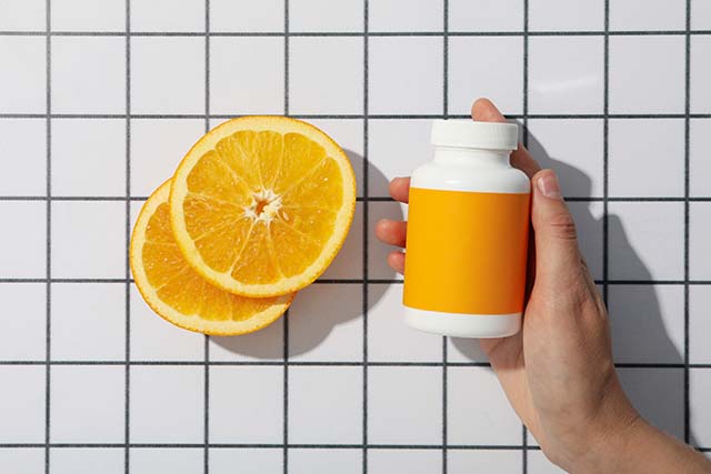 bote de vitamina C y gajos de naranja